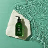 Green bottle of TO112 hand wash on white marble coaster floating in water